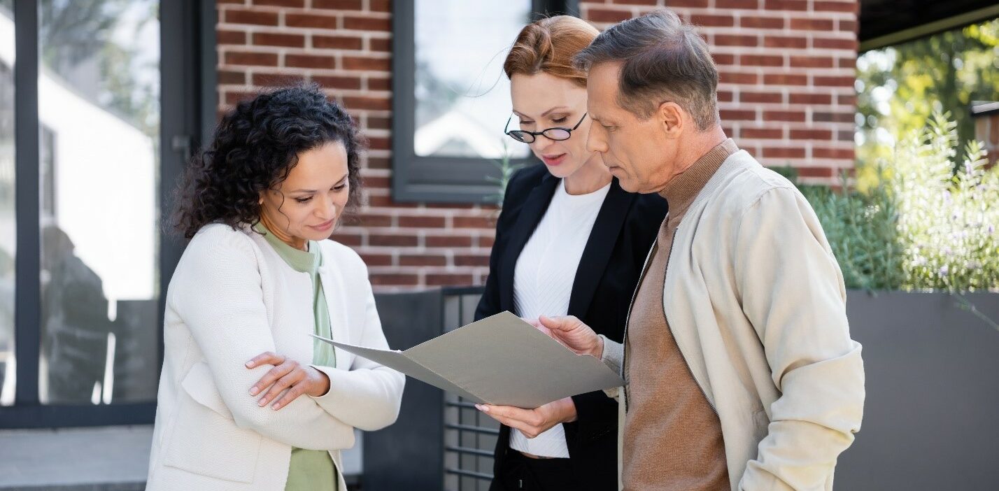 A man and woman standing with a real estate agent reading papers
